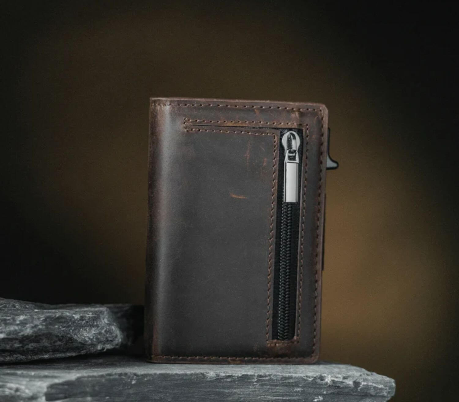 Brown men’s leather wallet with zipper pocket displayed on stone surface in a rugged, durable style.