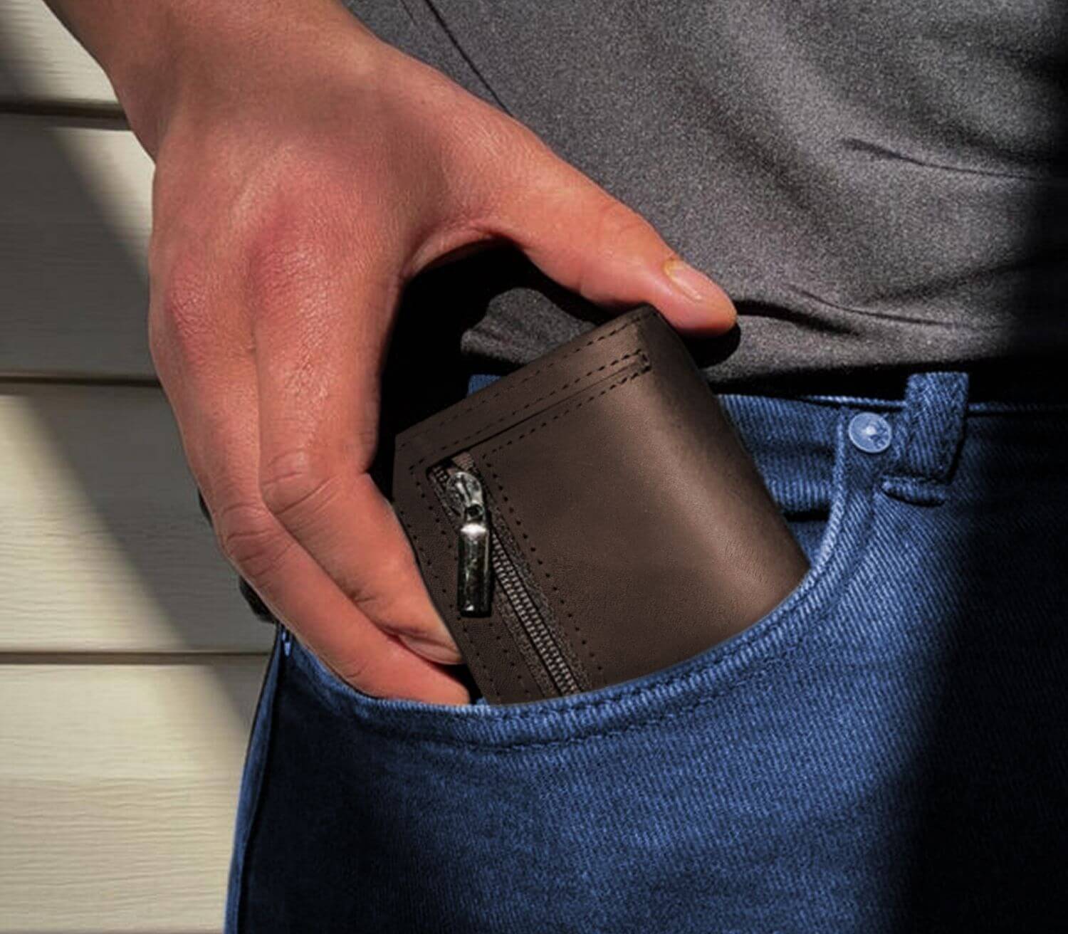 Brown men’s slim leather wallet with zipper pocket being placed into jeans pocket for everyday use.
