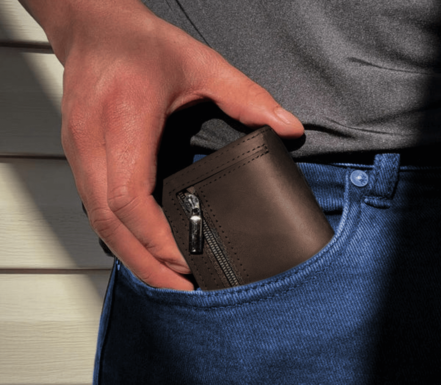 Brown men’s slim leather wallet with zipper pocket being placed into jeans pocket for everyday use.