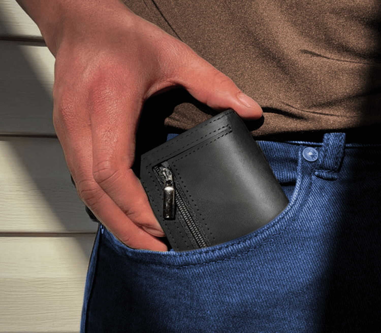 Black men’s slim leather wallet with zipper pocket being placed into front jeans pocket for everyday carry.