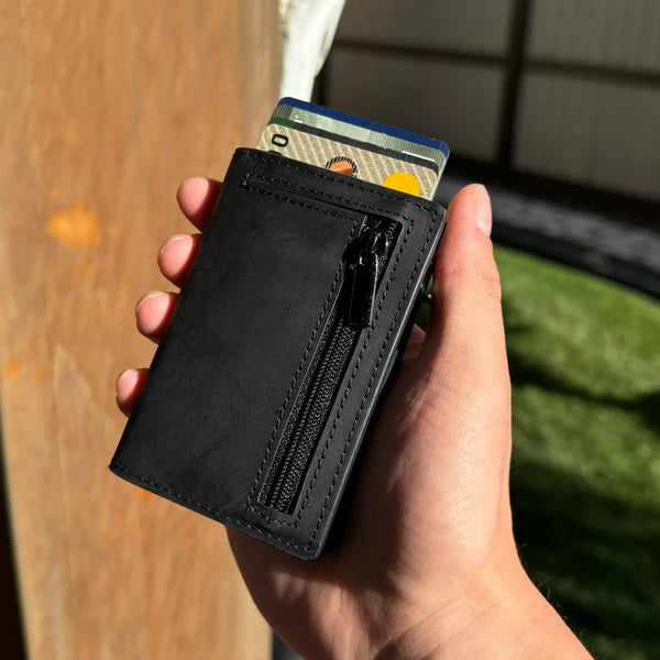 Hand holding a black cardholder wallet with a zipper and cards visible.